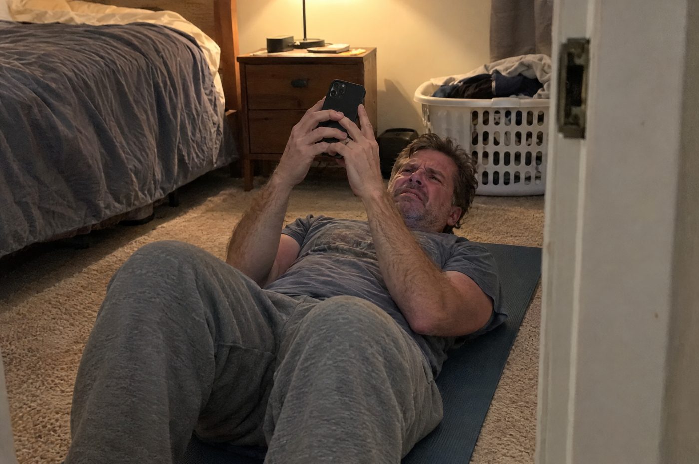 A man lying on a yoga mat doing kegels from a phone app, confused