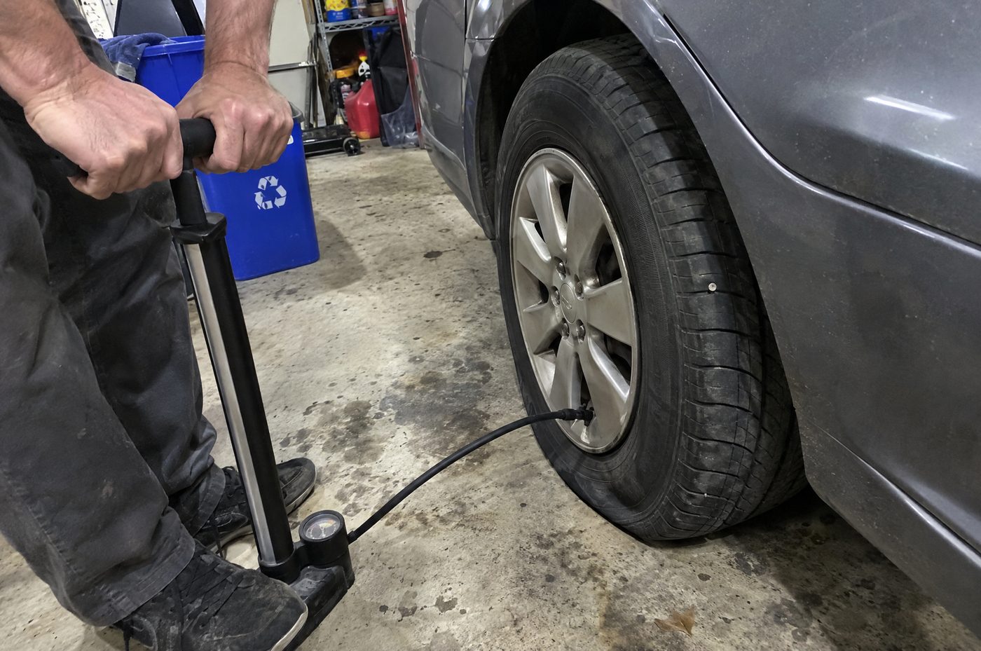 A man pumping air into a car tire with a nail stuck in it
